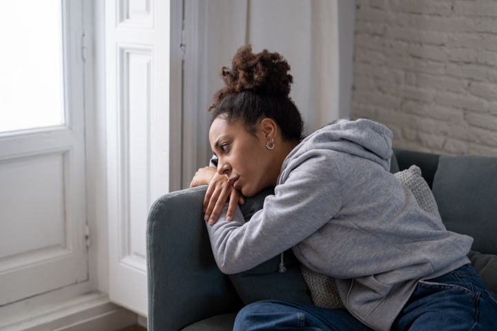 Lonely young afro latina young woman on sofa feeling in pain, exhaustion and sadness. Depressed hispanic or afro american girl at home, looking away with sad expression. In Mental health concept.
